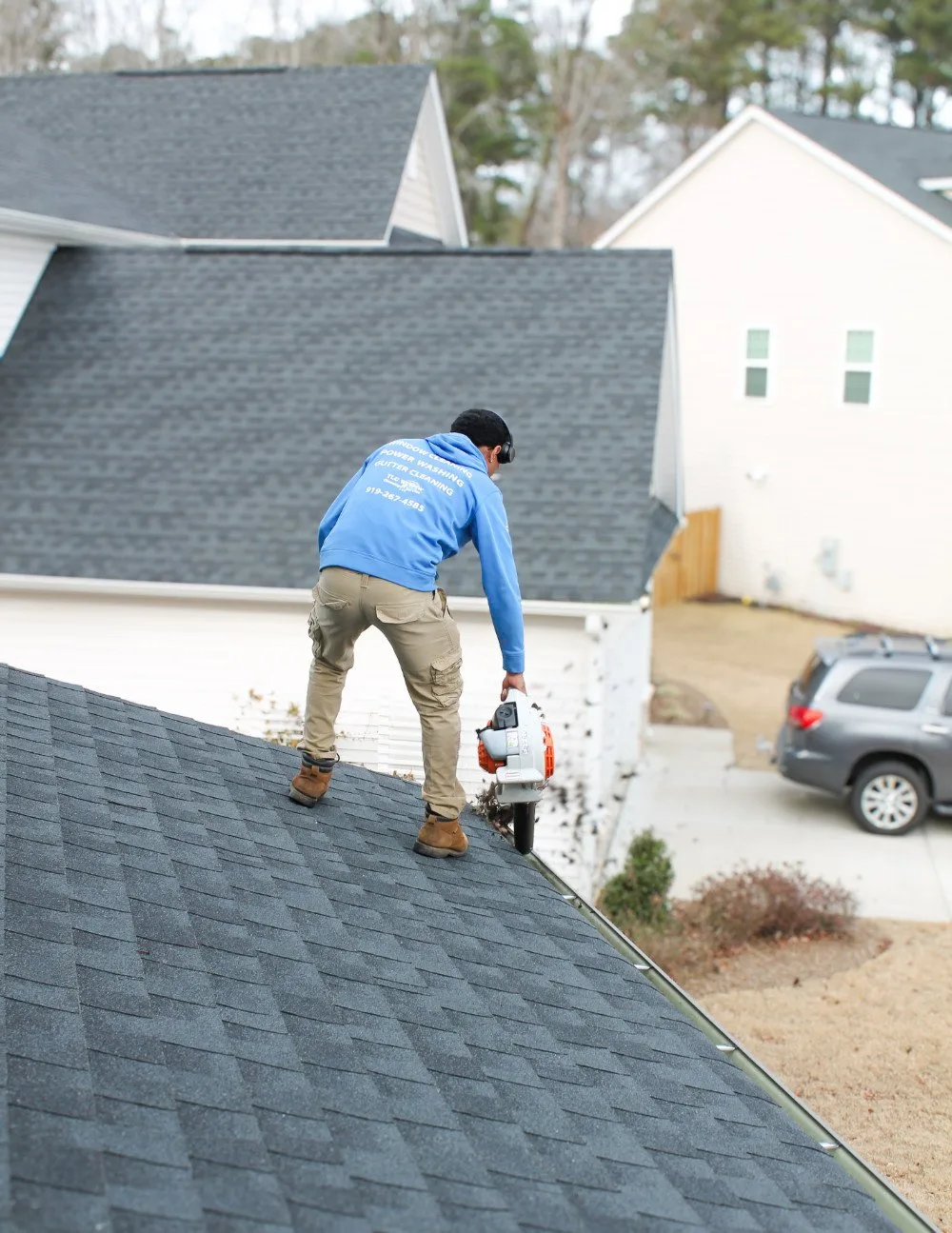 Professional gutter cleaning technician clearing leaves and debris from residential gutters in North Carolina