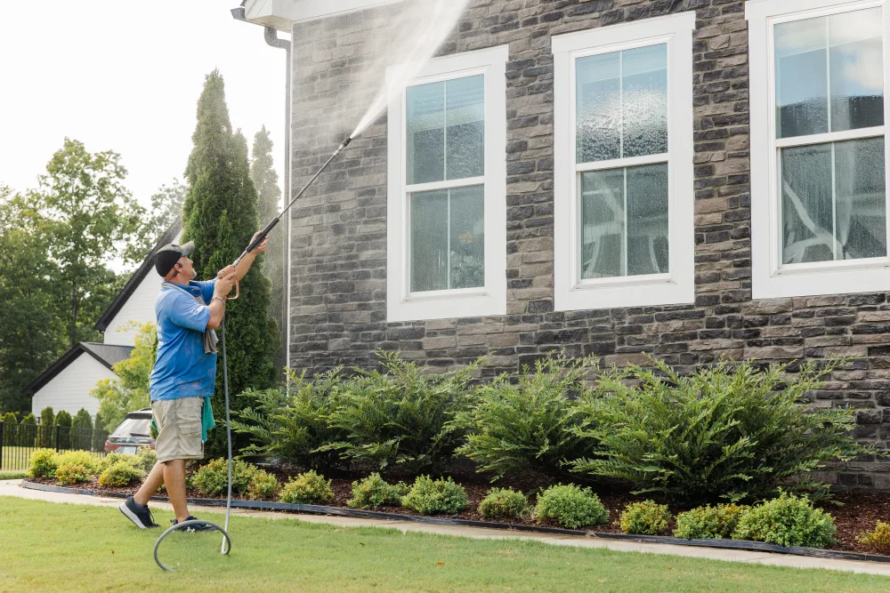 TLC Exterior Cleaning technician house washing the stone exterior and windows of a home in Holly Springs, NC